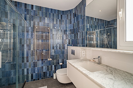 浴室的墙壁上铺有两种单色调的深蓝色大理石瓷砖 带大理石台面 镜子和水槽上方小窗的方形水槽 对面是带玻璃栏杆的淋浴房背景图片