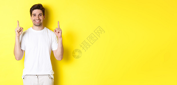 穿白色T恤衫的帅哥举起手来 展示购物报价 站在黄色背景上站立学生标识成人促销情绪技术工作室快乐手势闲暇时尚高清图片素材