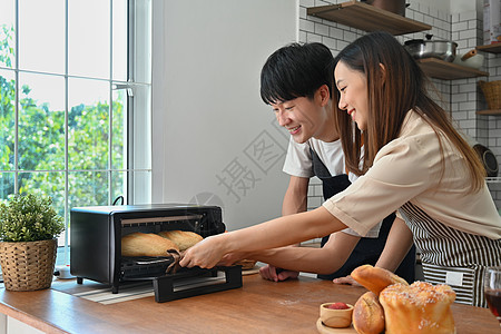 美丽的年轻夫妇在烤箱中烤面包 在现代厨房内一起准备早餐 (笑声)图片