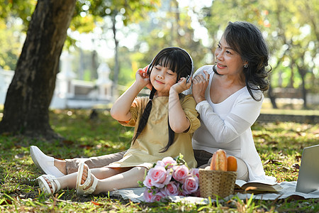 在夏季公园与祖母野餐时 戴着耳机听音乐的可爱亚洲小女孩 家庭 休闲概念图片