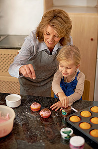 和奶奶一起在厨房玩得开心 一个小姑娘 在祖母的帮助下装饰了纸杯蛋糕 她妈妈也帮她图片