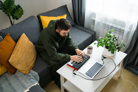 男子音乐制作人或编曲人使用笔记本电脑和 midi 键盘和其他音频设备在家庭工作室创作音乐 击败制作和安排音频内容和创作歌曲概念音图片