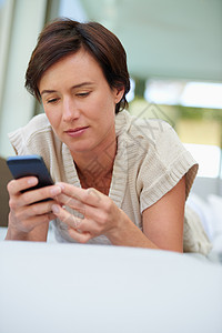 给朋友发短信 一个有魅力的女人 在家里躺在沙发上时用她的手机图片
