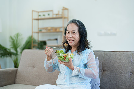 老年健康一位年长的亚洲妇女通过吃沙拉来照顾自己的健康家庭桌子祖母夫妻成人烹饪老年午餐微笑厨房背景