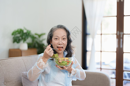 一位年长的亚洲妇女通过吃沙拉来照顾自己的健康成人祖母桌子老年烹饪退休蔬菜水果家庭食品图片