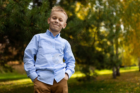 在秋天森林的背景下 一个穿着蓝衬衫的快乐男孩 双手在口袋中站立着 站在他身上图片