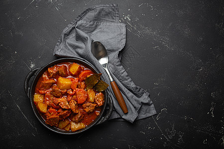 牛肉炖土豆 胡萝卜和美味的肉汁 放在黑色砂锅锅里 用月桂叶和勺子放在黑色深色乡村混凝土背景上 从上面看 文字空间午餐烧烤桌子食物图片