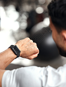 一名混血男子在健身房训练时用空白显示屏检查他的数字手表的特写镜头 上面的家伙在手臂上佩戴健身追踪器以监测进度 心率和卡路里图片