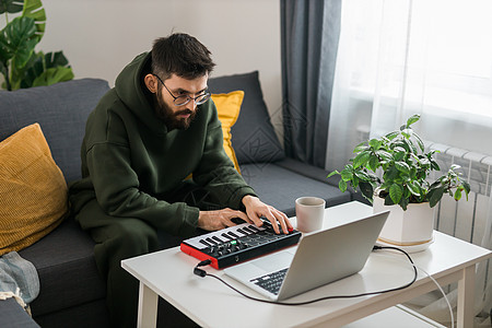男子音乐制作人或编曲人使用笔记本电脑和 midi 键盘和其他音频设备在家庭工作室创作音乐 击败制作和安排音频内容和创作歌曲概念软图片
