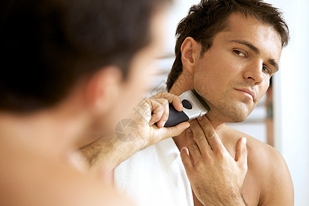 年轻男子用电剃须刀照镜子刮胡子的反射图片