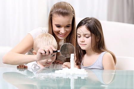 带着孩子的妇女透过放大镜在桌子上观望着一个有孩子的妇女白色乐趣活动玩具兄弟家庭孩子们游戏保姆绿色图片