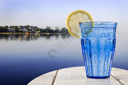 a 蓝色玻璃 在木甲板上加闪光水和柠檬 俯视热带缓冲带的平静水饮食海洋假期娱乐矿物天空饮料水果反射情调图片