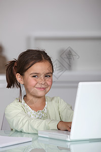 小女孩坐在笔记本电脑上学校桌子黑发家庭作业女孩学习办公室微笑童年玻璃图片