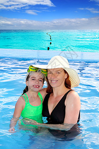 在热带海滩的游泳池中 母亲和女儿抱抱蓝色帽子童年地平线旅行闲暇通体拥抱女性游泳衣图片