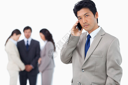 认真的商务人士在手机上与随行团队在他身后图片
