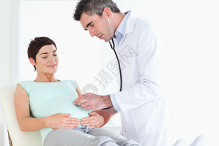 医生用听诊器监听女人的腹部诊所孕产药品职业说谎病人医院孕妇装工作治疗图片