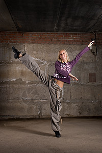在灰砖墙上跳舞的美丽舞女演员慢跑鞋跳跃女士裤子运动说唱运动鞋姿势夜生活图片