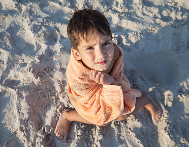 小男孩在沙沙滩上坐着毛巾包着小男孩童年男性海岸线橙子海岸假期支撑孩子海滩闲暇图片