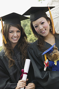 两名持有文凭和泰迪熊肖像的毕业生图片