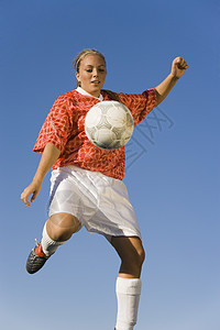 年轻的女足球运动员在蓝天上踢足球图片