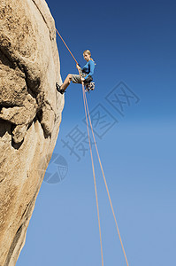 一位年轻女子从悬崖上爬到清蓝天空的低角度视角图片