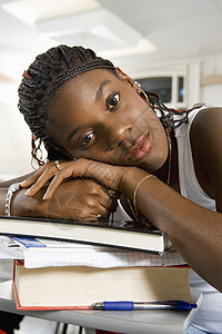 无聊的非裔美国年轻女子在课堂上躺在一堆书本上休息图片