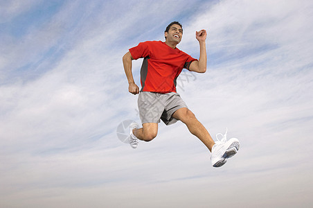 一位男性运动员的低角度 在中空对着天空和云层奔跑图片