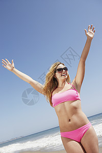 在海滩上穿粉红色比基尼的无爱抚的年轻女子图片