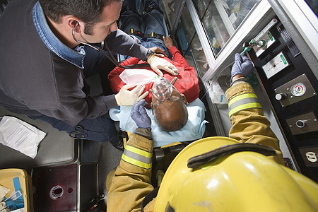 男消防员和急救队医生在救护车中照顾一名受伤的老年男子图片