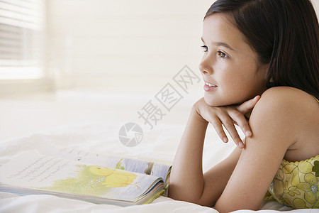 快乐的小女孩白天在床上看故事书时做白日梦沉思就寝童年幸福水平闲暇阅读孩子们想像力故事图片