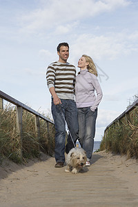 快乐的一对夫妇与狗一起在海滩上徒步步行图片