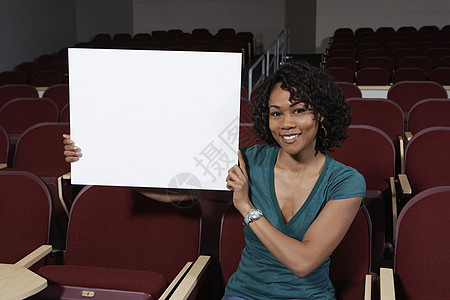 坐在教室椅子上拿着广告牌的快乐美丽女性的画像图片