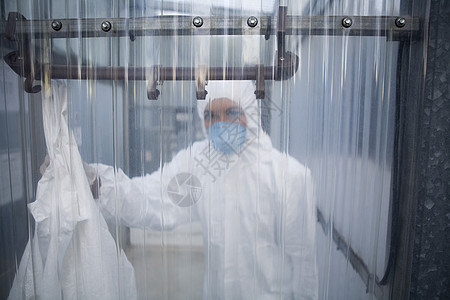 实验室塑料墙后穿戴防护面具和防伪服的女工肖像图片