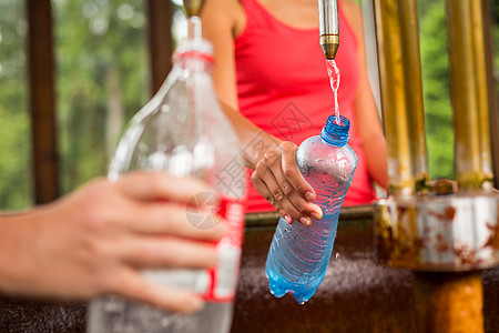 年轻女子用健康的矿泉水装上塑料瓶子矿物治疗喷泉温泉蒸汽荣耀疾病橙子地热饮料图片