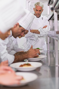 主厨 看着一排大厨 把意大利面盘和叶烧熟面条双臂制服商业女性男性职业伙伴台面餐厅图片