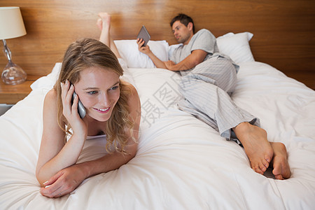 使用移动电话的妇女和床上有数字石板的男子软垫男性手机卧室闲暇呼唤夫妻拨号触摸屏电话图片
