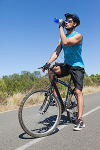 英俊的骑自行车的人在他的自行车饮用水上休息一下晴天蓝天活动娱乐环境男人山地冒险家勘探瓶子图片