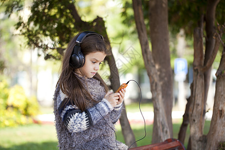 美丽的小女孩在耳机上收听音乐节目快乐头发女孩女儿手机女性歌曲脸蛋黑发孩子图片