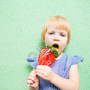 美丽的小女孩拿着草莓状棒棒棒糖快乐女孩乐趣食物漩涡女性微笑辫子糖果美食图片