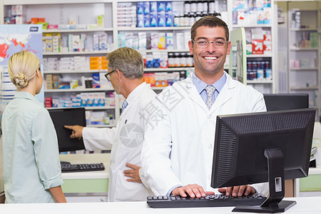 快乐的药剂师看着相机疾病医疗女士技术诊所处方贮存药剂男性工作服图片