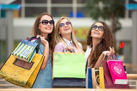 3个漂亮女孩戴着墨镜和购物袋购物狂购物者微笑团体开支顾客朋友们礼物女性买家图片