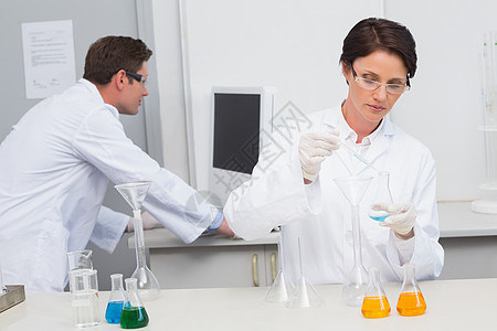 科学家将化学液排入漏斗 她的同事在计算机方面工作图片
