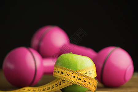 粉红哑铃 配有绿苹果和测量磁带绿色减肥营养木头饮食健康饮食体育锻炼卷尺桌子粉色背景图片