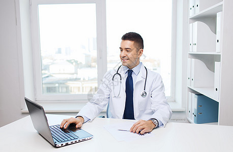 男医生在医疗办公室用膝上型笔记本电脑诊所专家办公室男性帮助医疗保险保健微笑从业者拉丁图片