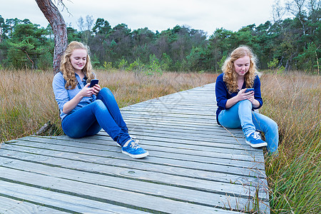 两名女孩在性质上操作移动电话;图片