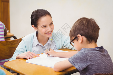 老师在课堂上帮助一个小男孩桌子学习女性学校童年同学们快乐教育男生小学图片