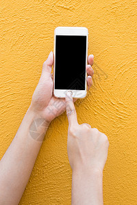 黄色墙背景上手持白色智能手机女士屏幕展示互联网细胞女性电脑办公室空白公司图片