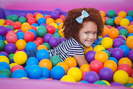 在海绵球池里笑笑的可爱女孩水池喜悦童年快乐乐趣混血派对娱乐性微笑女性图片