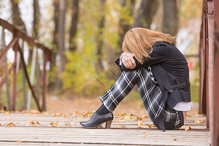 悲伤的女孩坐在桥上 头靠在膝上躺着图片