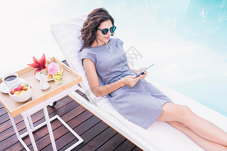 使用数字平板电脑的美丽年轻女子阅读技术女士滚动晴天沟通太阳椅自由饮料裙子图片